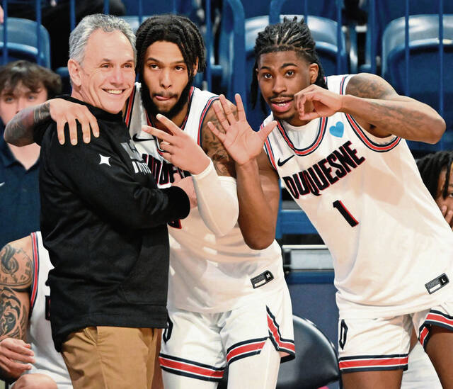Duquesne’s Dae Dae Grant and Jimmy Clark III (1) celebrate with head coach Keith Dambrot after beating George Mason for Dambrot’s 500th win Wednesday, Feb. 8, 2023, at UPMC Cooper Fieldhouse.