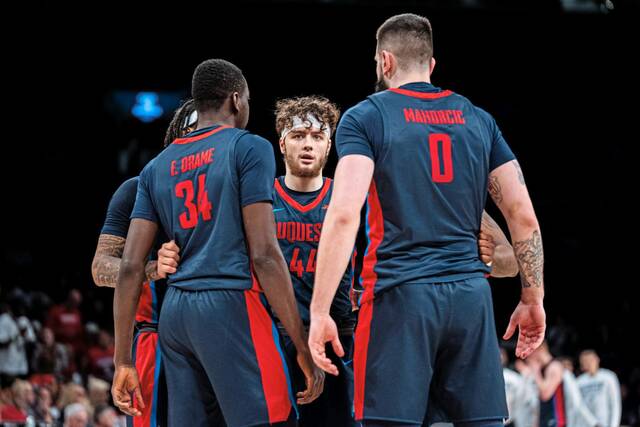 Duquesne’s Jake DiMichele (center) huddles with teammates Dusan Mahorcic and Fousseyni Drame during the first half of the Atlantic 10 championship game Sunday.