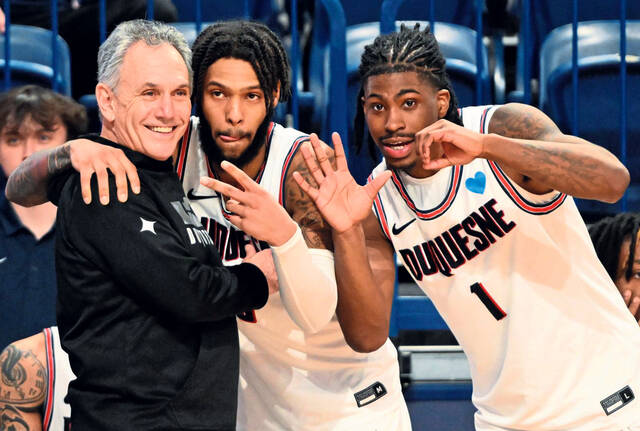 Duquesne’s Dae Dae Grant and Jimmy Clark III (1) celebrate with head coach Keith Dambrot after beating George Mason for the coach’s 500th win in 2023 at UPMC Cooper Fieldhouse.