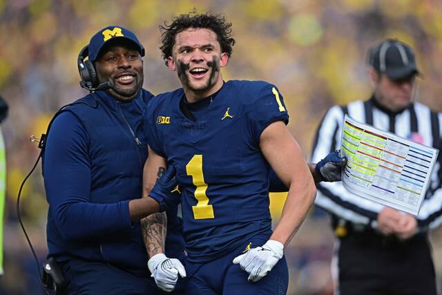 Michigan wide receiver Roman Wilson is grabbed by acting head coach Sherrone Moore after video replay confirmed his touchdown in a Nov. 25, 2023, game in Ann Arbor, Mich.